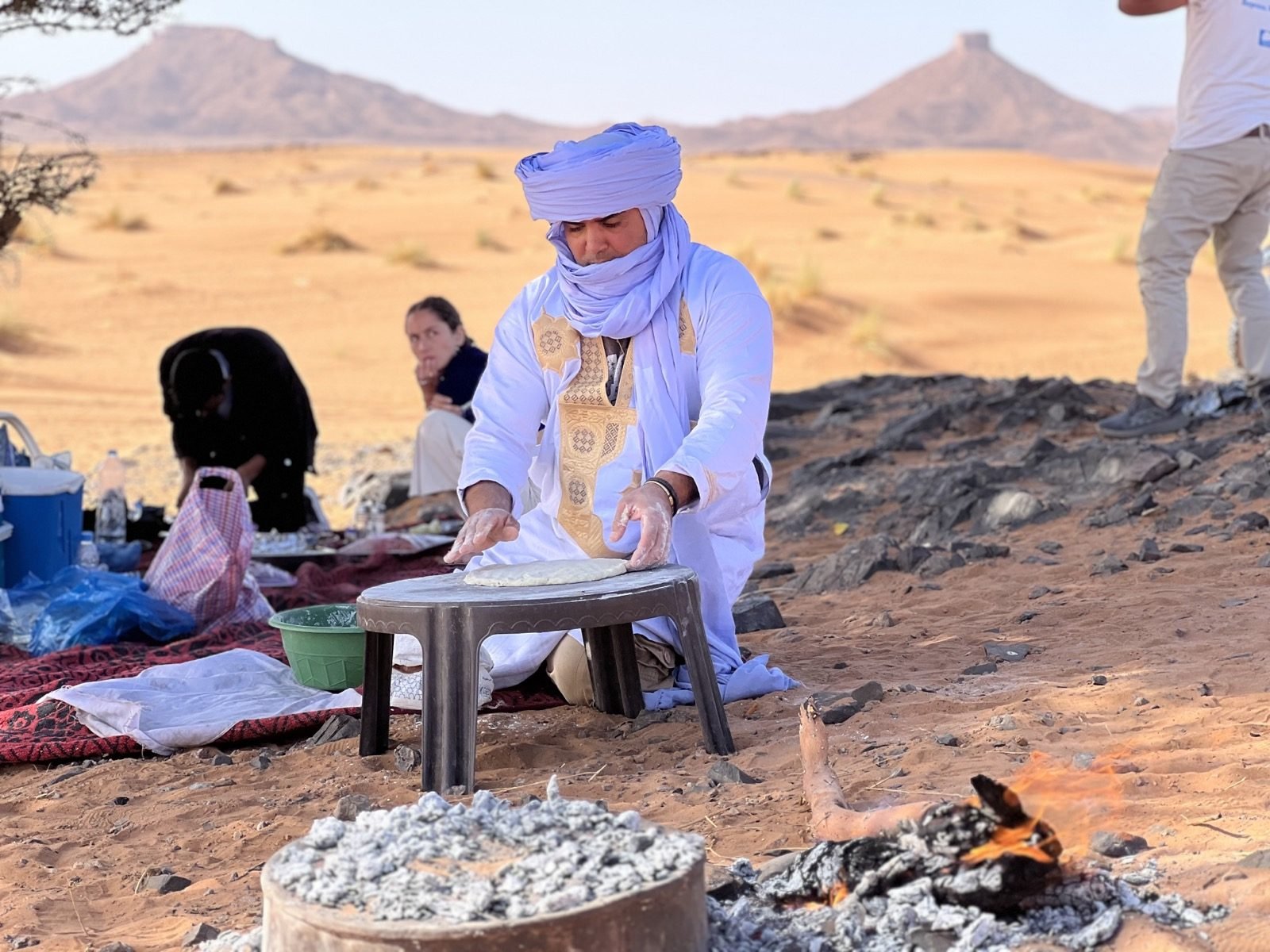 A Berber guide baking traditional desert bread as travellers watch in the Sahara